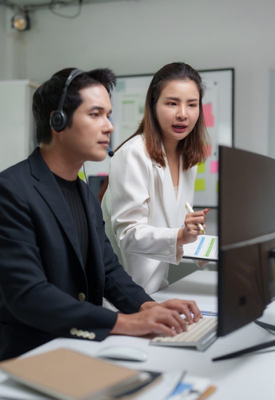 Two asian businesspeople are working together in the office, using a computer and analyzing data on a clipboard, collaborating on a project