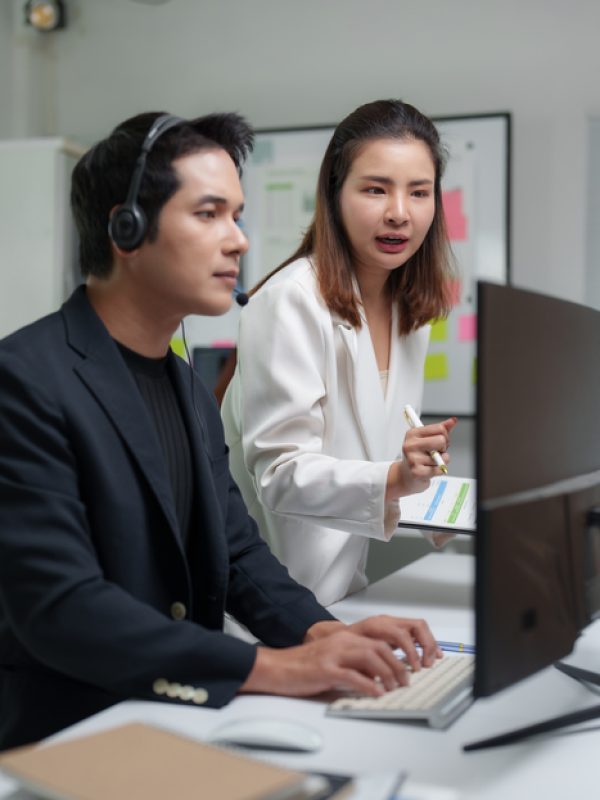 Two asian businesspeople are working together in the office, using a computer and analyzing data on a clipboard, collaborating on a project