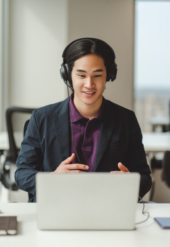 Portrait of confident Asian businessman, call center operator in headset, using laptop, having video call. Attractive Japanese manager working in modern office. Business concept