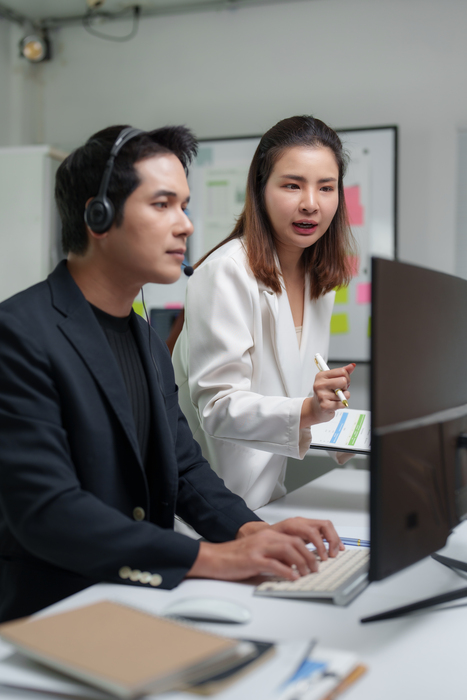 Two asian businesspeople are working together in the office, using a computer and analyzing data on a clipboard, collaborating on a project