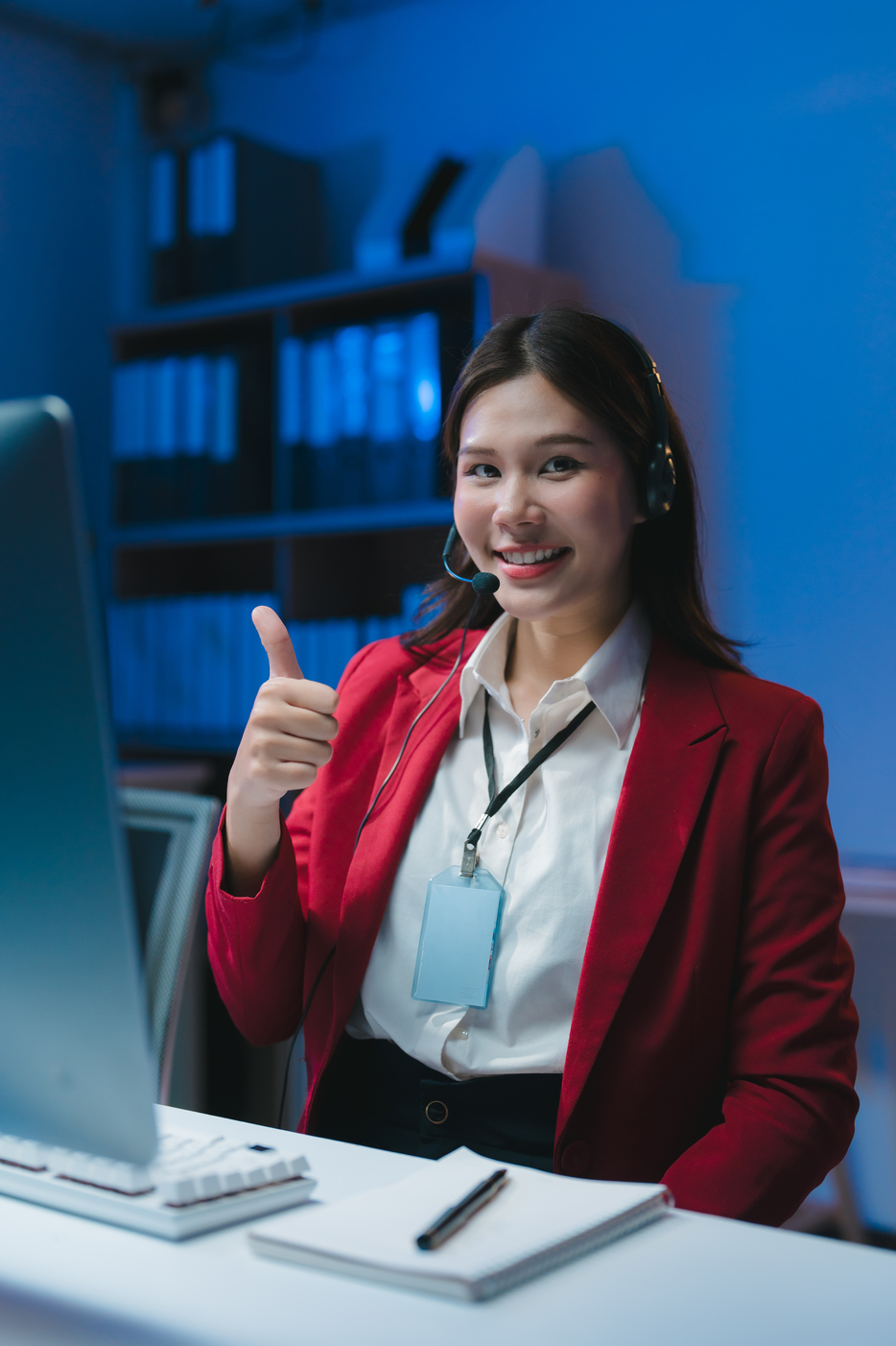 Young asian customer service representative working late at night in office showing thumbs up