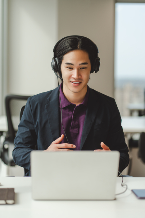 Portrait of confident Asian businessman, call center operator in headset, using laptop, having video call. Attractive Japanese manager working in modern office. Business concept